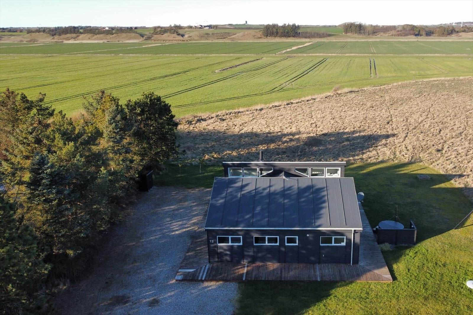 Ein Haus mit Garten steht in einer ländlichen Umgebung mit grünen Feldern und einem Wald.