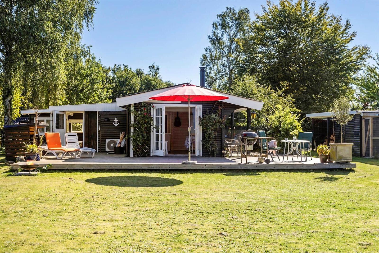 House with wooden terrace, garden and barbecue area. Windows and door are open.