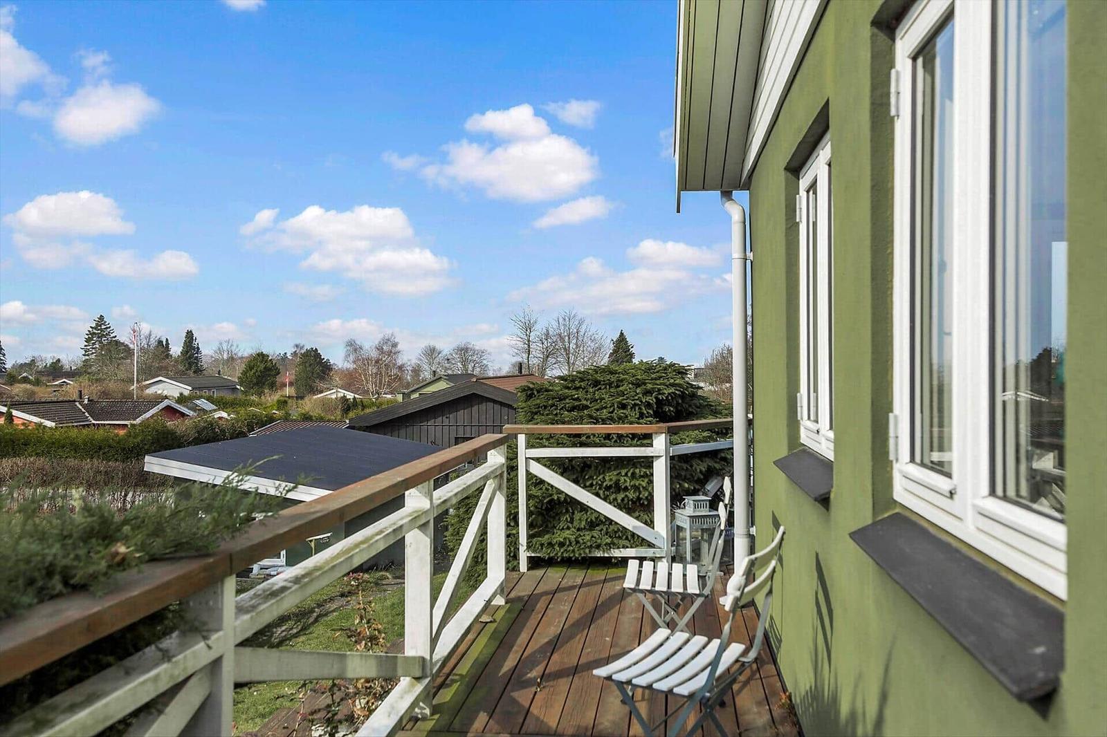 Green house with garden and terrace under blue sky.