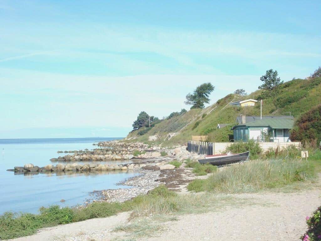 Strand mit Booten und Häusern auf grüner Anhöhe.