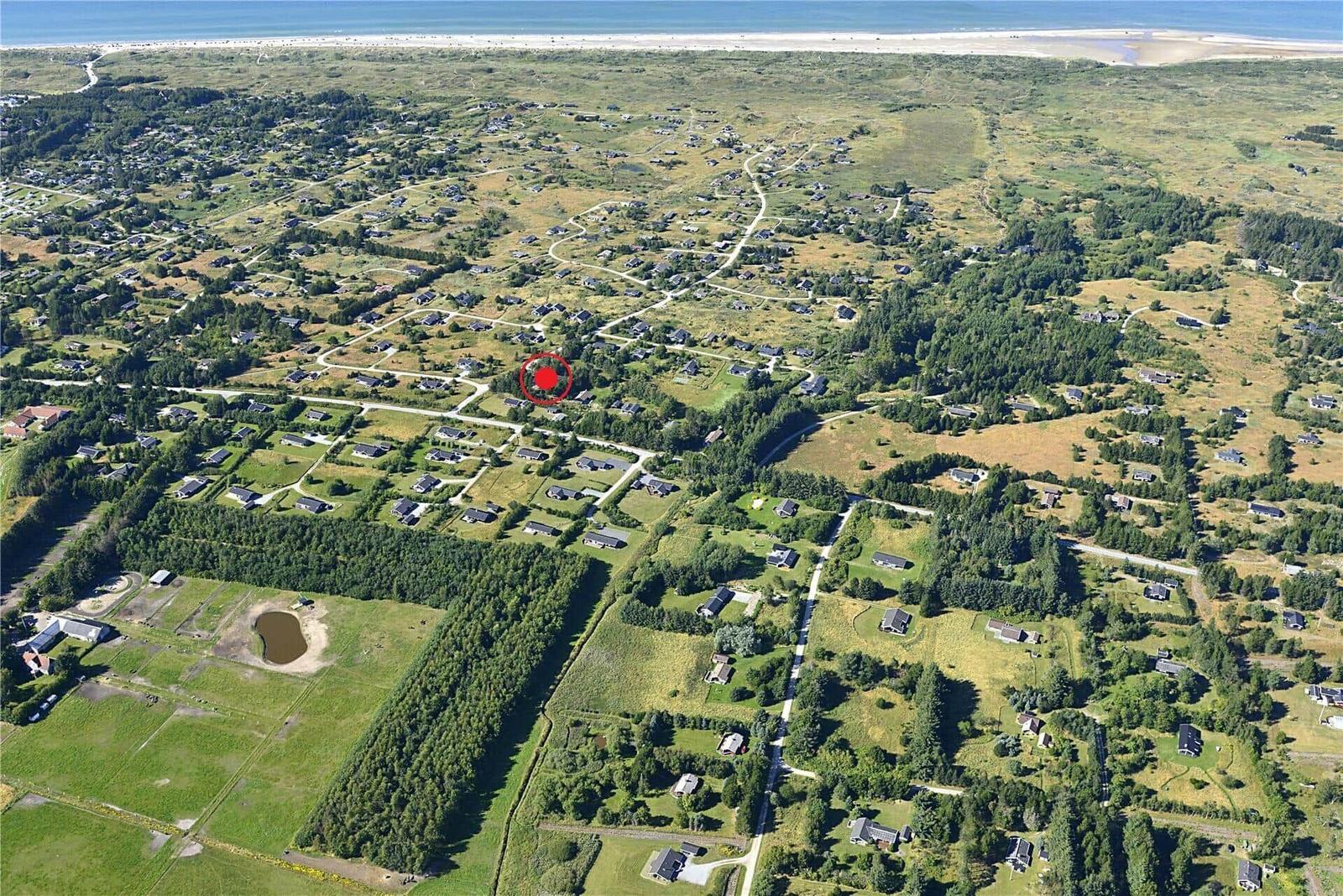 Luftbild eines Ferienhauses in einer grünen, ländlichen Umgebung mit Wald und Strand im Hintergrund.