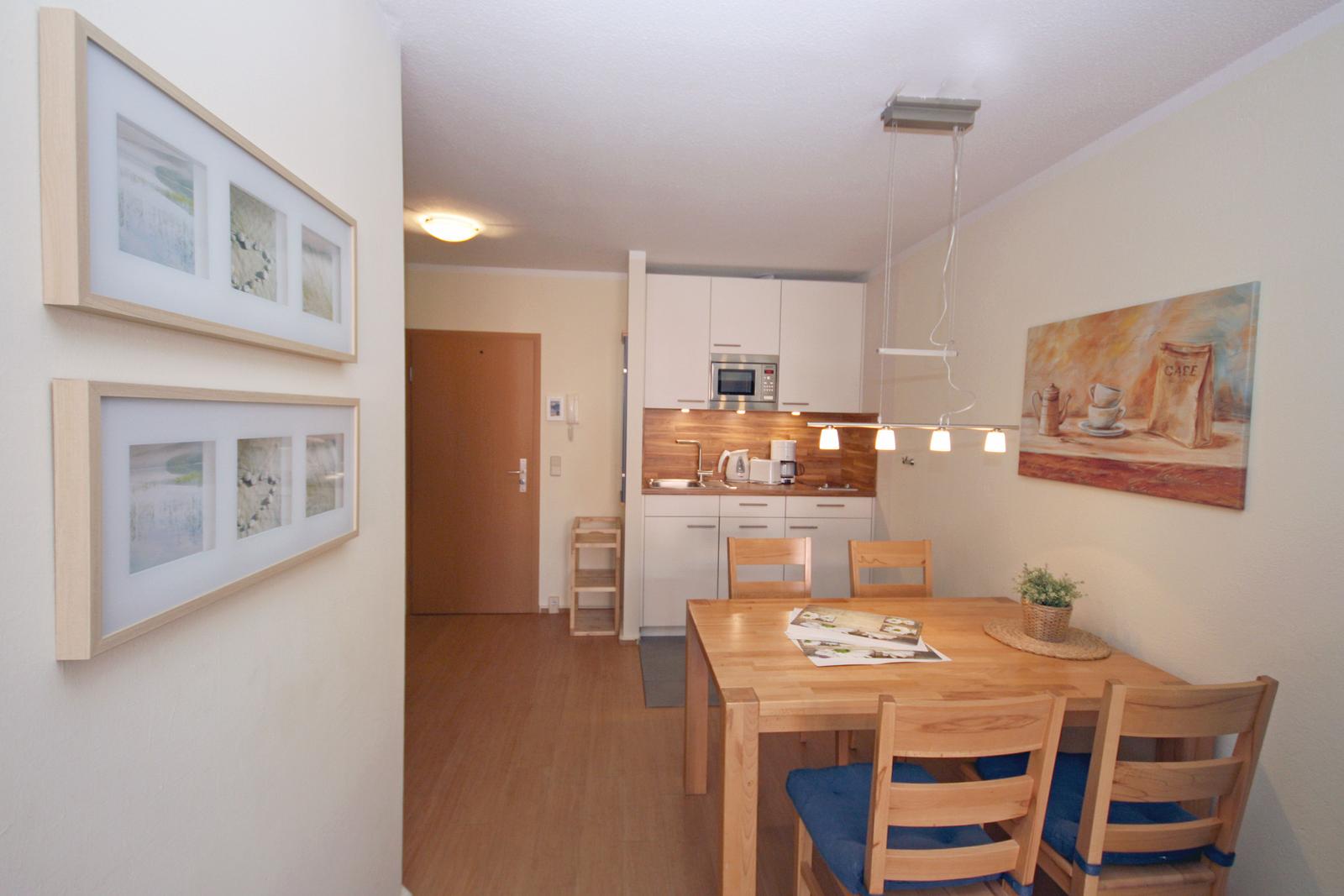 Dining area with wooden table and chairs, kitchen with white cabinets and wooden backsplash.