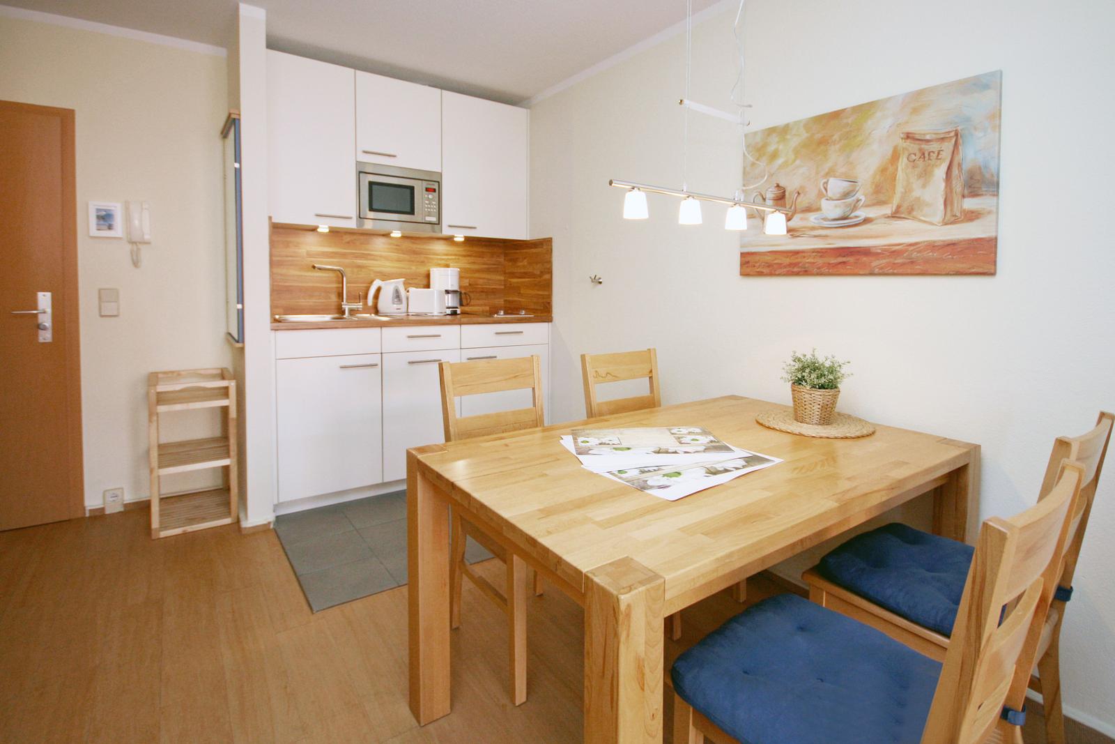 Dining area with wooden table and chairs, kitchenette with microwave and wall art.