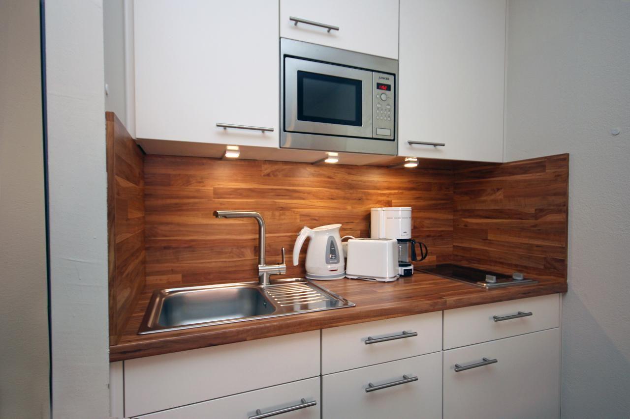 Kitchen with stainless steel sink, microwave, coffee machine, and wooden backsplash.