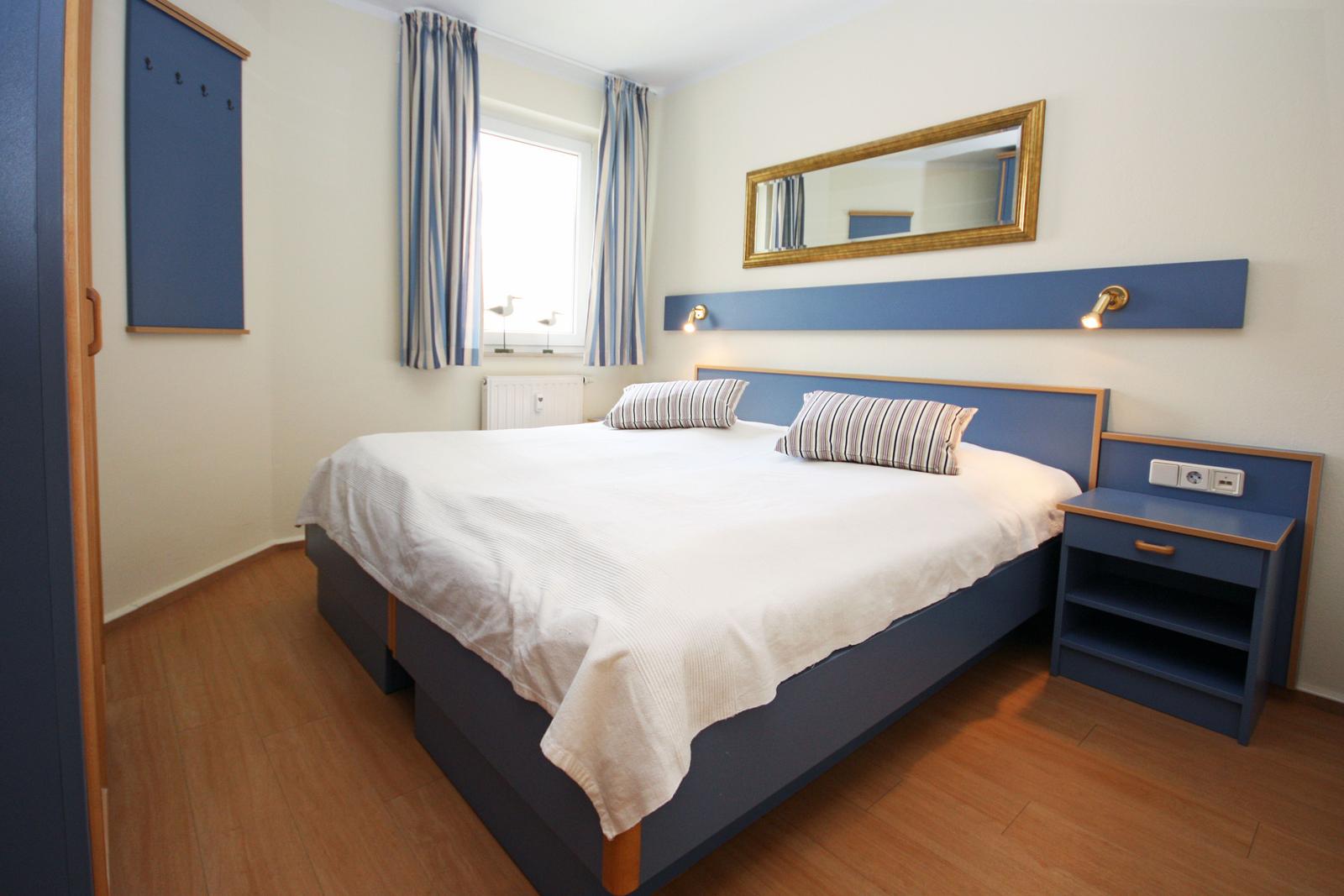 Bedroom with double bed, blue headboard and nightstand, mirror, and window with curtains.