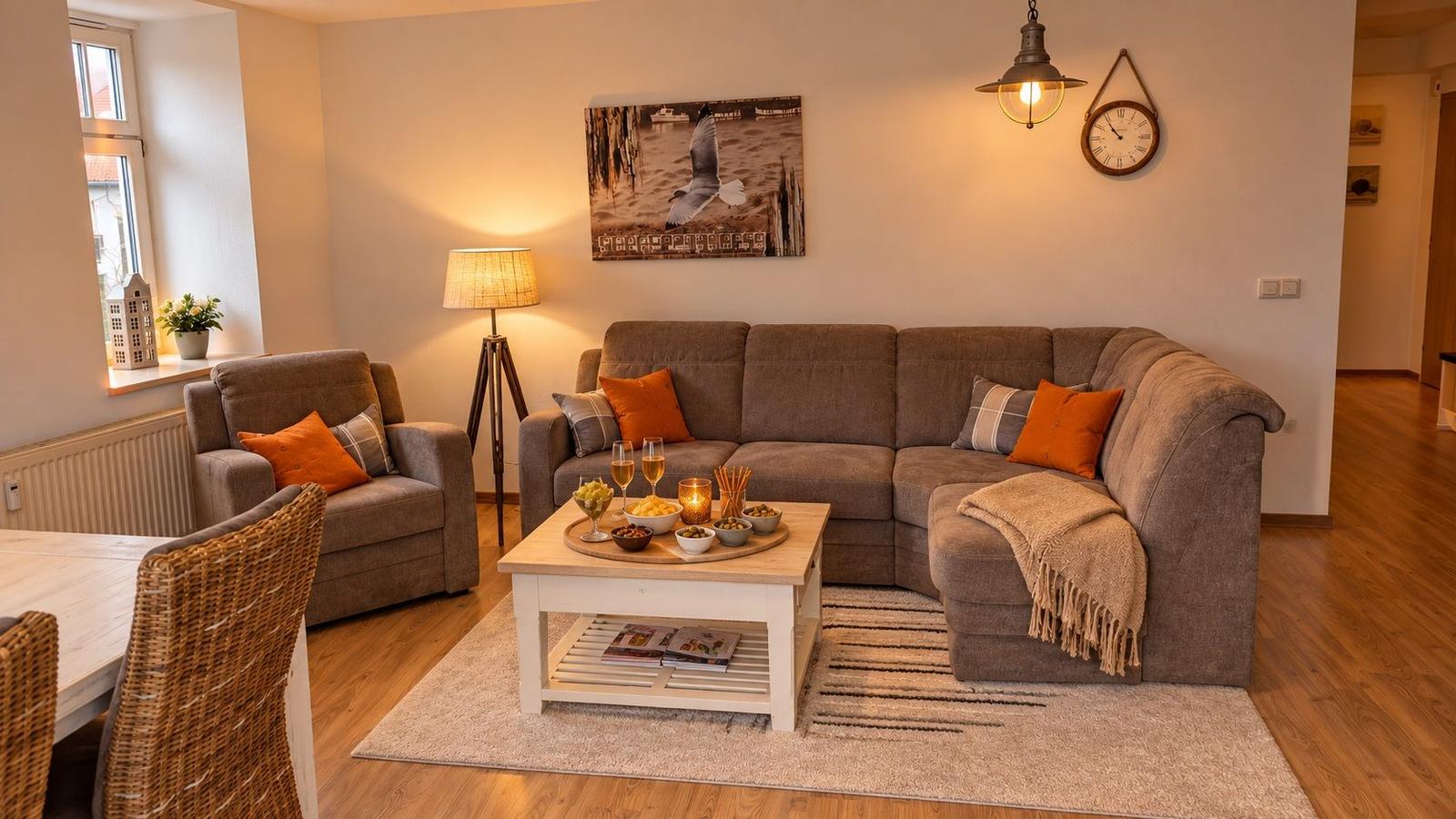 Living room with gray sofa, armchair, and wooden floor. A picture and a clock hang on the wall.