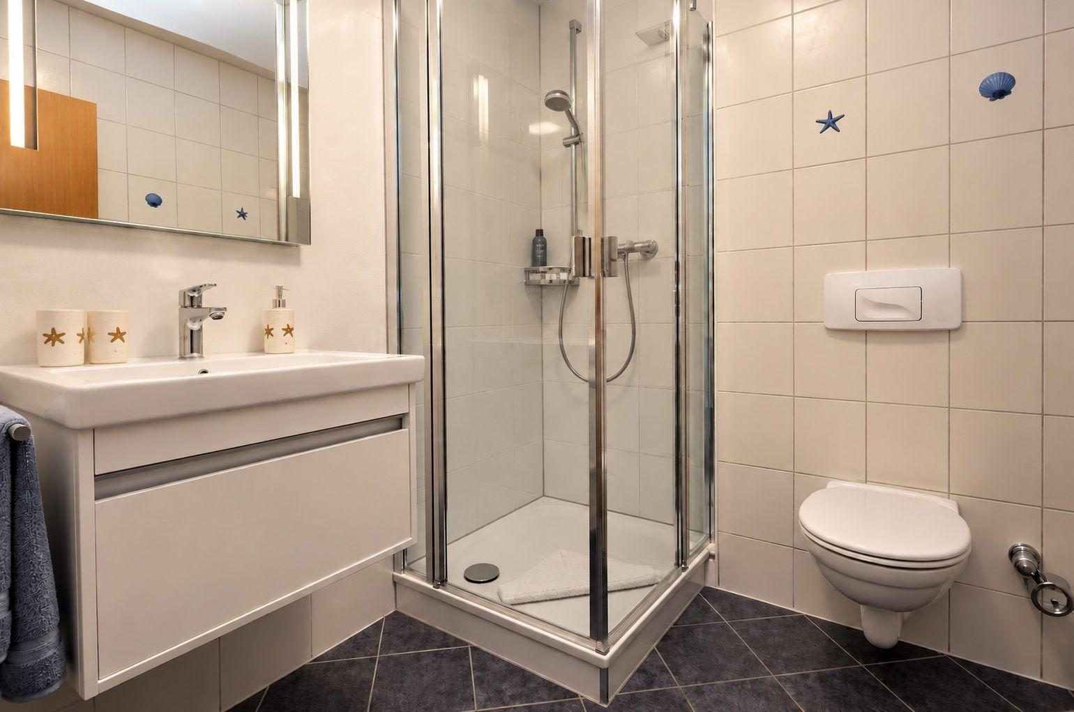 Badezimmer mit Dusche, Waschbecken und Toilette. Wandfliesen mit Muschel- und Sternmotiven.