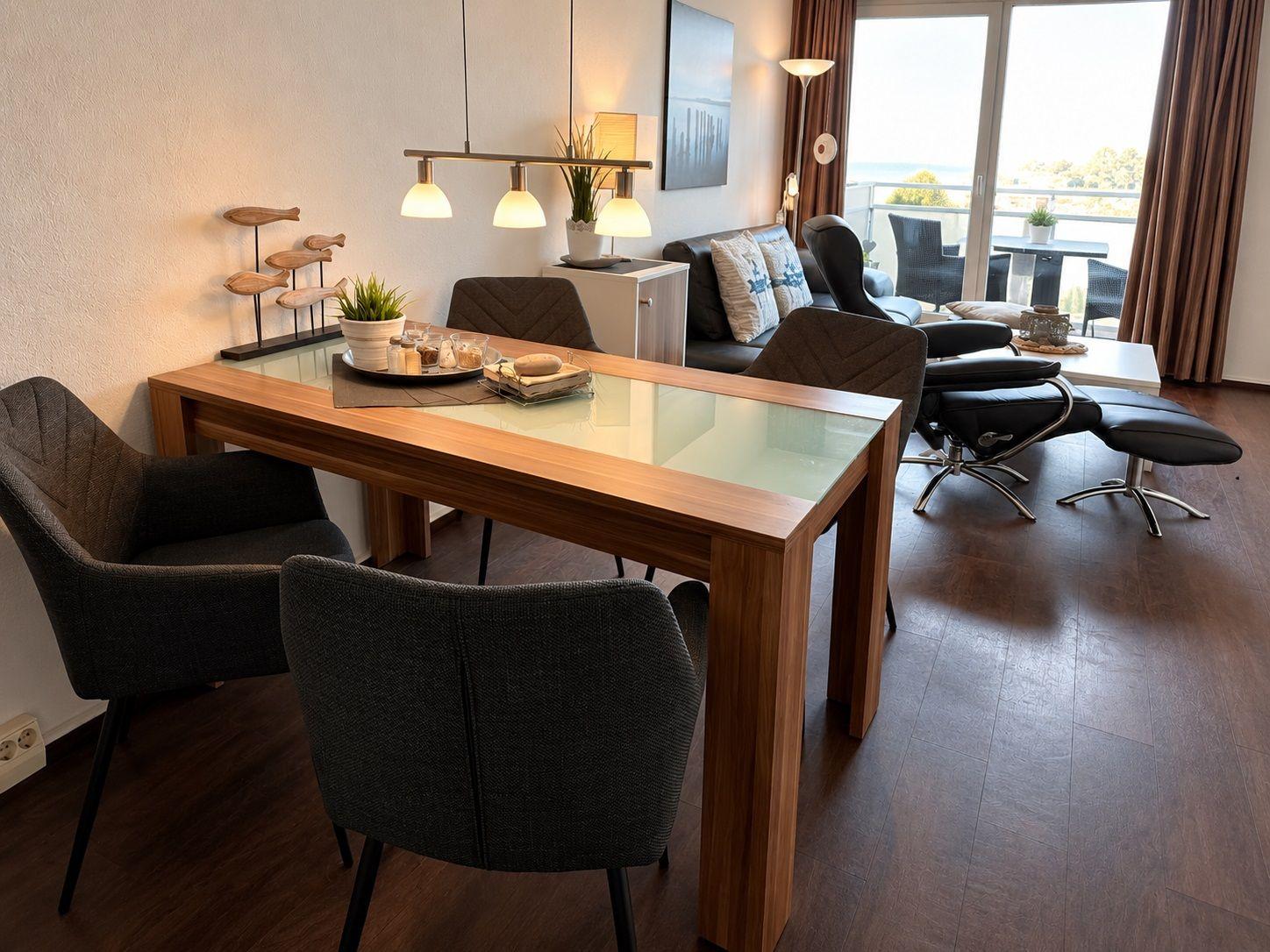 Wohnzimmer mit weißen Möbeln, Holzakzenten und Pflanze. Fernseher und Schrank sind vorhanden.
