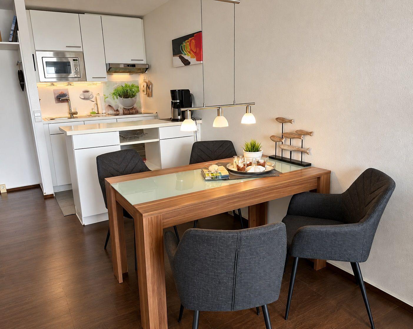 Essbereich mit Holztisch und Stühlen, Küche mit weißen Schränken und Edelstahlgeräten.