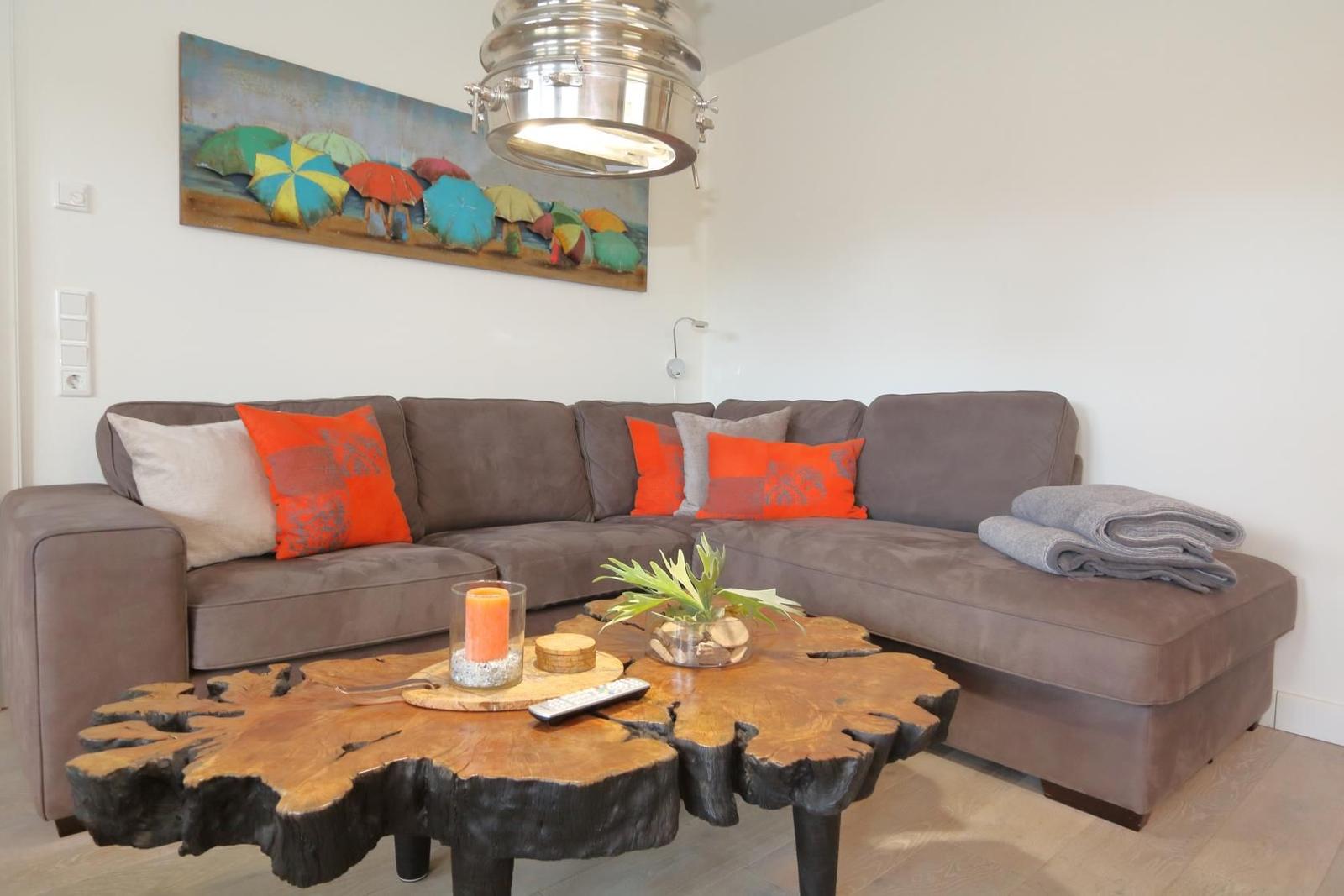 Holztisch mit Pflanze und Kerze im Wohnzimmer mit TV und Sitzgelegenheiten.