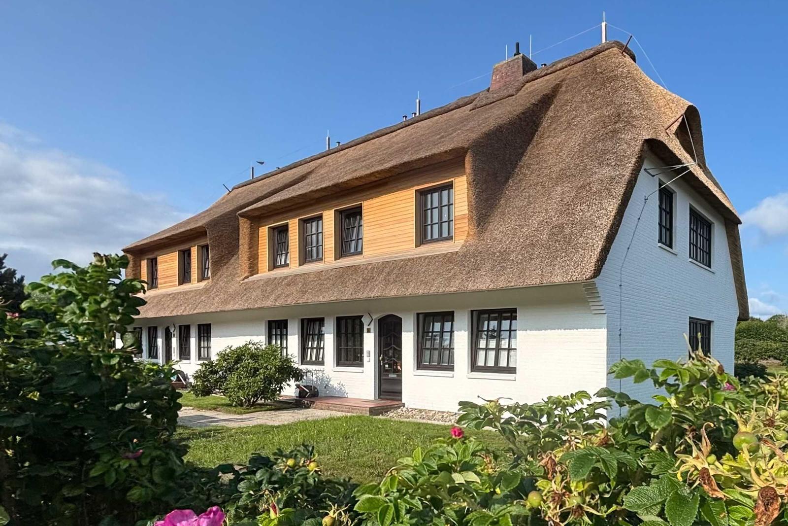 Terrasse mit Gartenmöbeln und Blick auf Haus mit Strohdach.