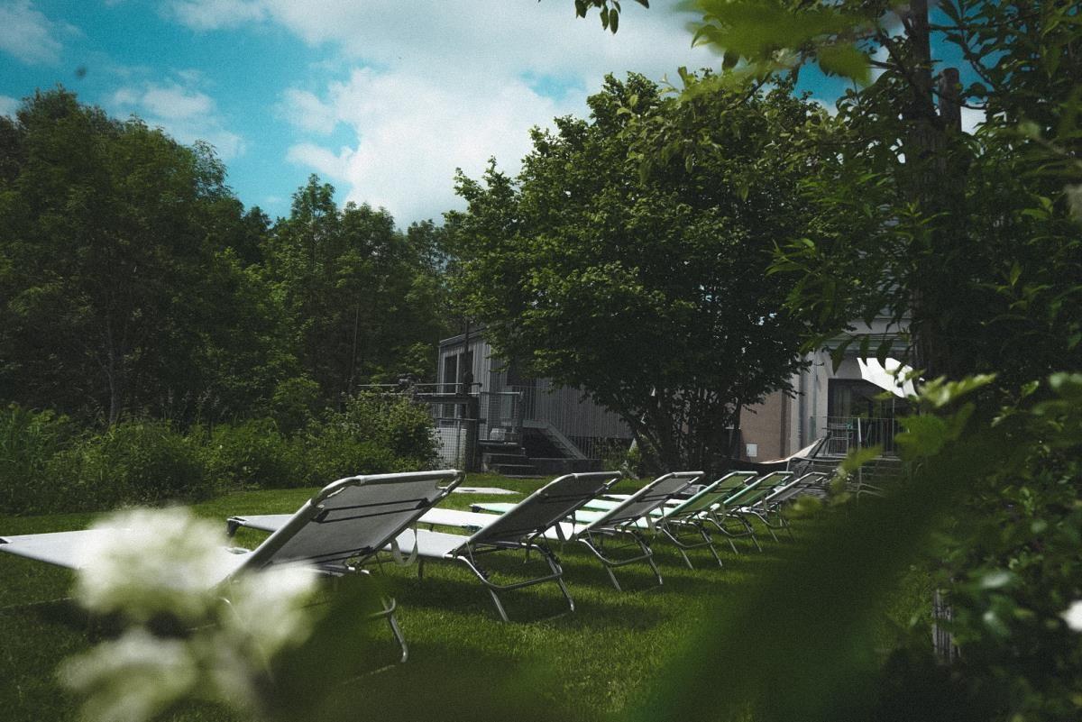 Grüner Garten mit Haus und Liegestühlen unter bewölktem Himmel.