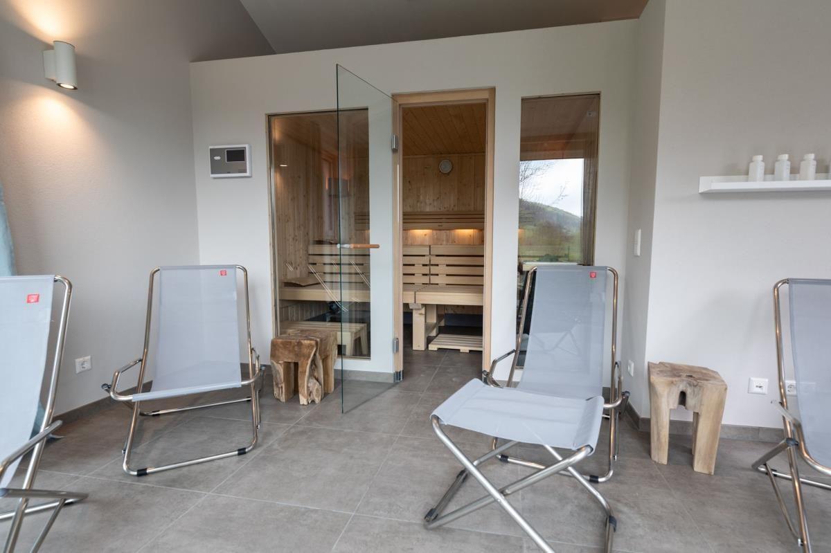 Eine Person in einem weißen Bademantel sitzt in einer Holzsauna mit Sitzbänken und einer Wandlampe.