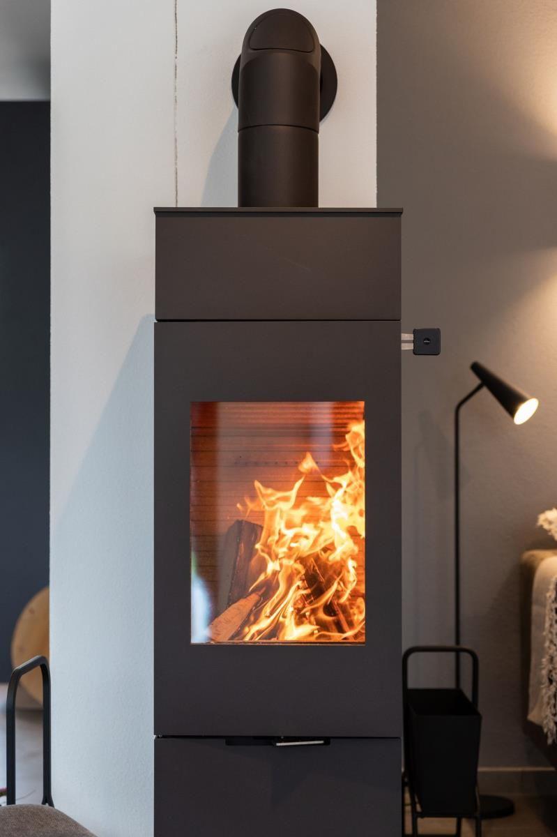 Ein Sessel steht vor einem Tisch mit Skulptur und Vasen. Eine Lampe leuchtet neben Vorhängen.