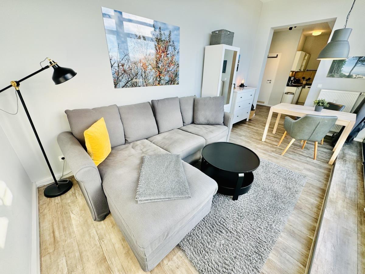 Schlafzimmer mit Bett, Fenster und TV. Blick in Wohnbereich mit Sofa und Tisch.