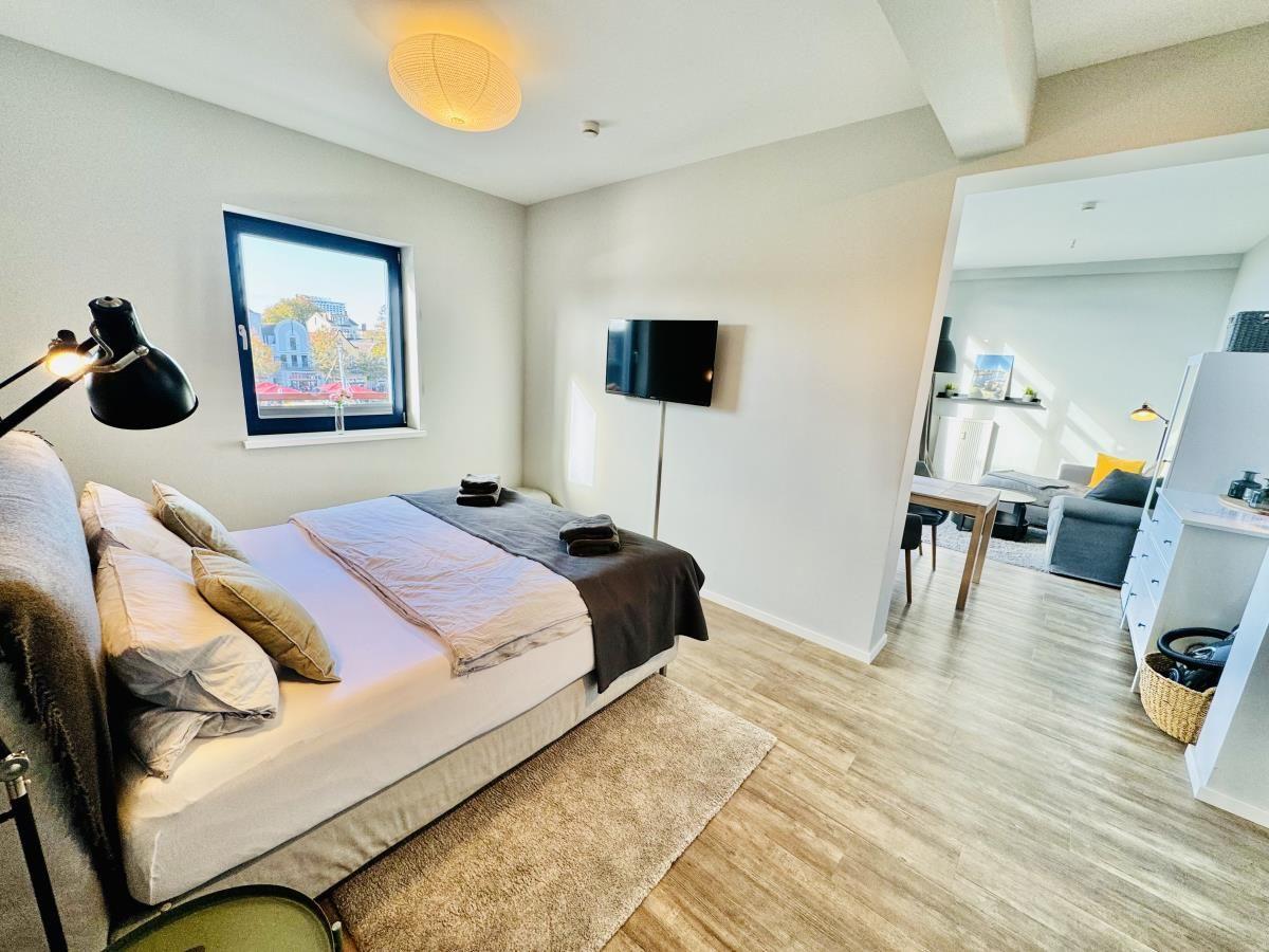 Schlafzimmer mit Doppelbett, Kleiderschrank und Küchenbereich im Hintergrund.