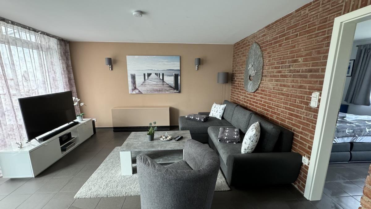 Wohnzimmer mit grauem Sofa, Couchtisch und Sessel vor Backsteinwand.
