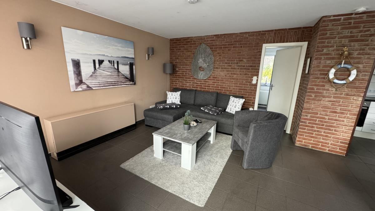 Essbereich mit Tisch und Stühlen, Küche im Hintergrund, Wandbild und Pflanzen.