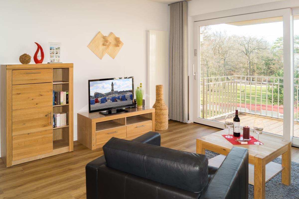 Wohnzimmer mit Ledersofa, Holztisch und Balkonblick auf Grünflächen.