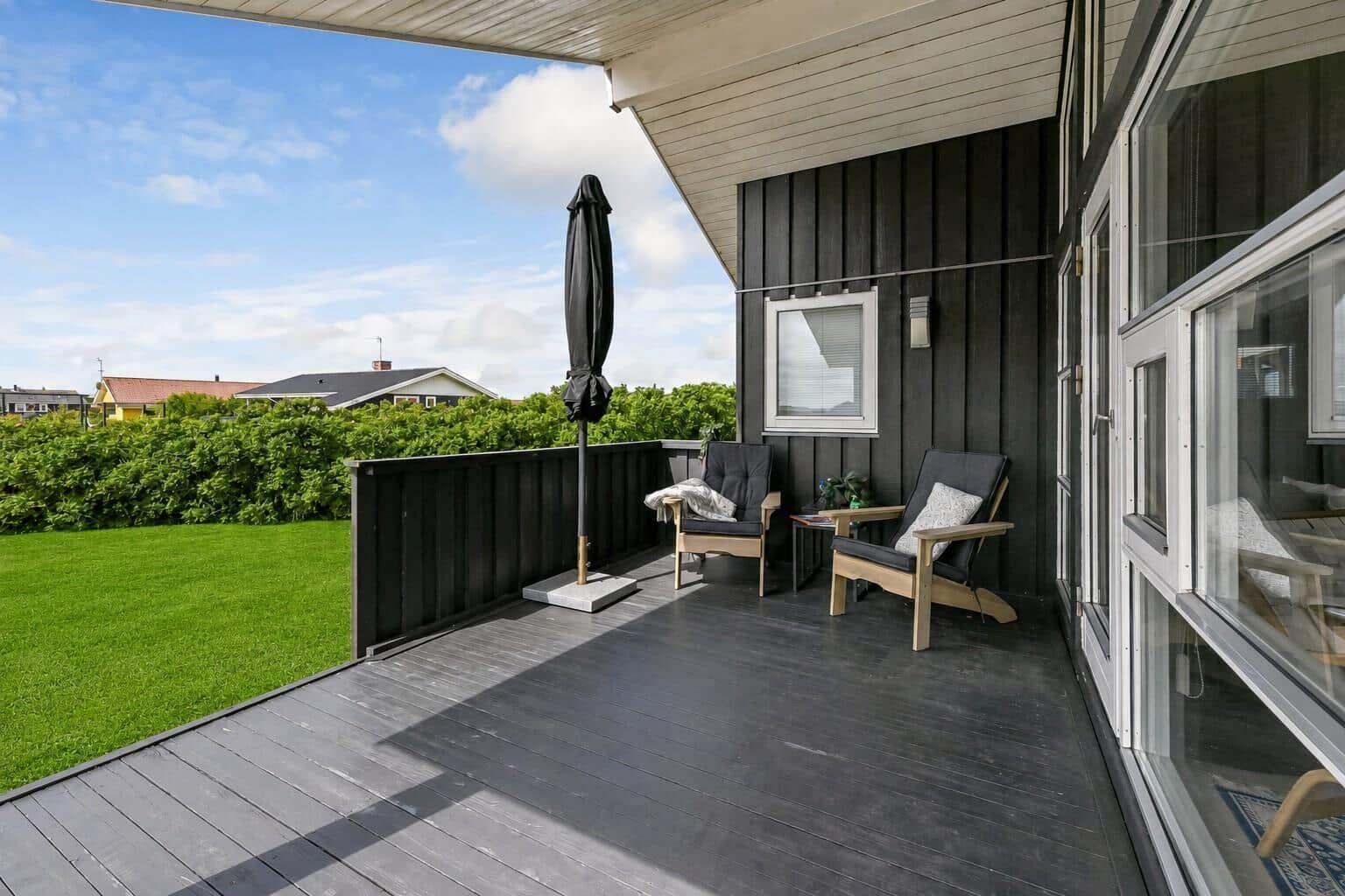 Terrasse mit Picknicktisch, gelben Sitzkissen und Liegestühlen. Hintergrund: Garten und Häuser.