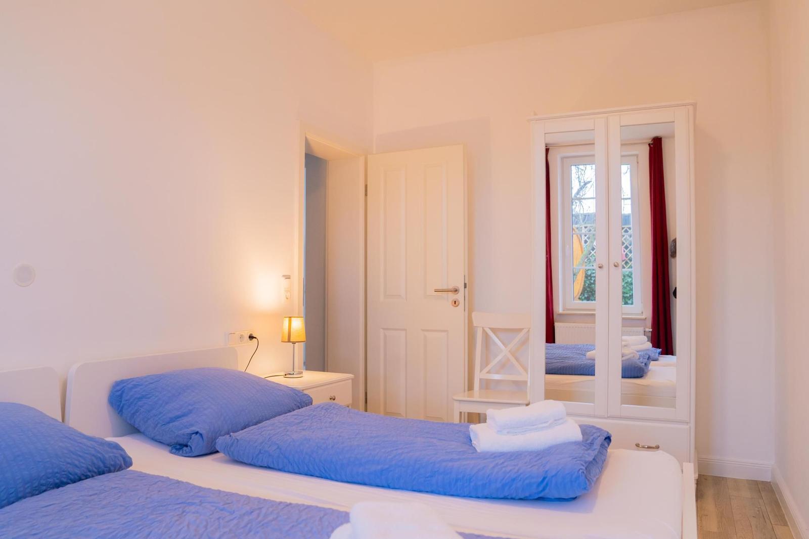 Zwei Betten mit blauen Bettwäsche und weißen Handtüchern. Fenster mit roten Vorhängen.