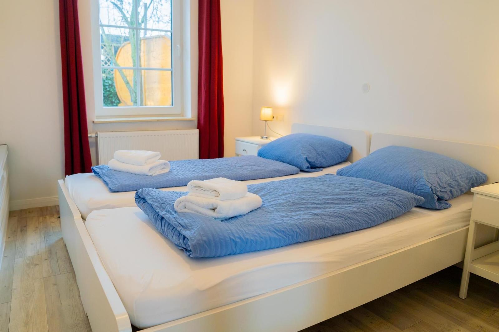Ein Raum mit einem weißen Doppelstockbett, blauen Bettwäsche und einem Fenster mit rotem Vorhang.