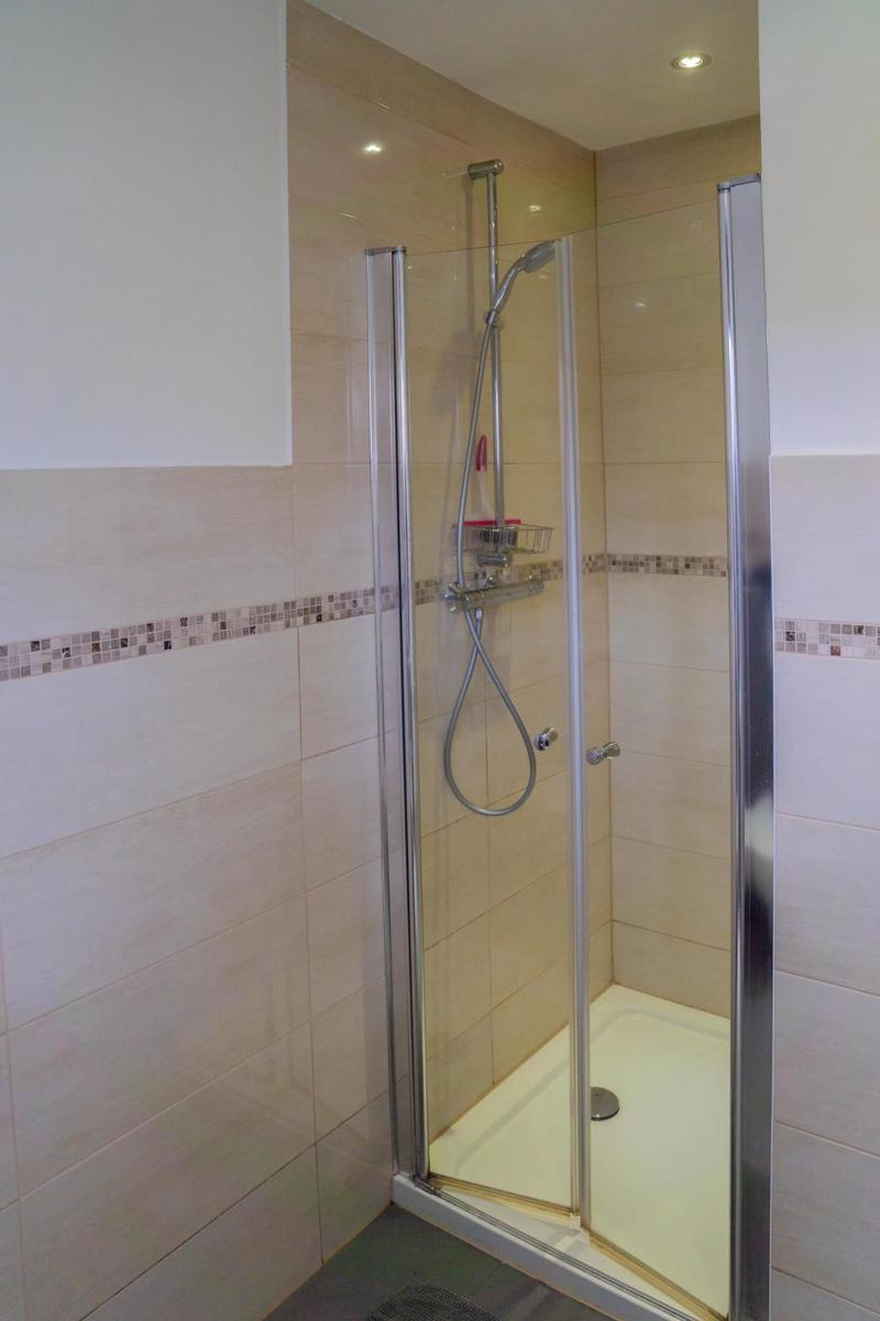 Badezimmer mit Dusche, Waschbecken und Fenster.