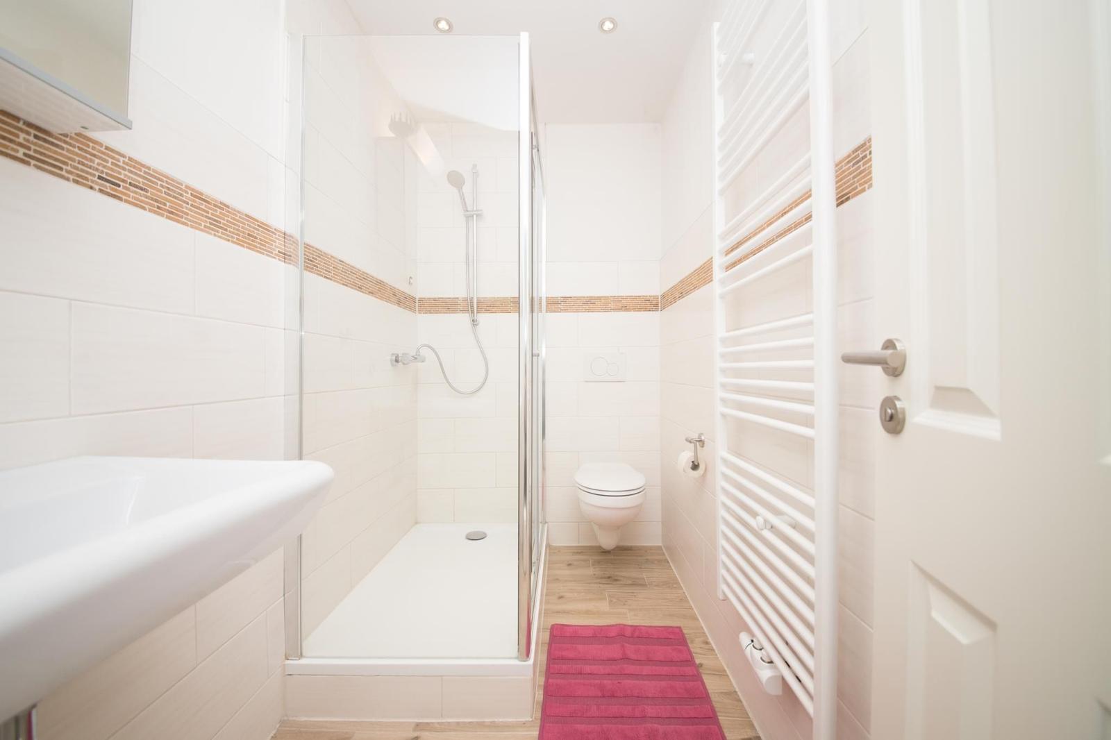 Bathroom with sink, mirror, and shower. Tiled wall and wooden floor.