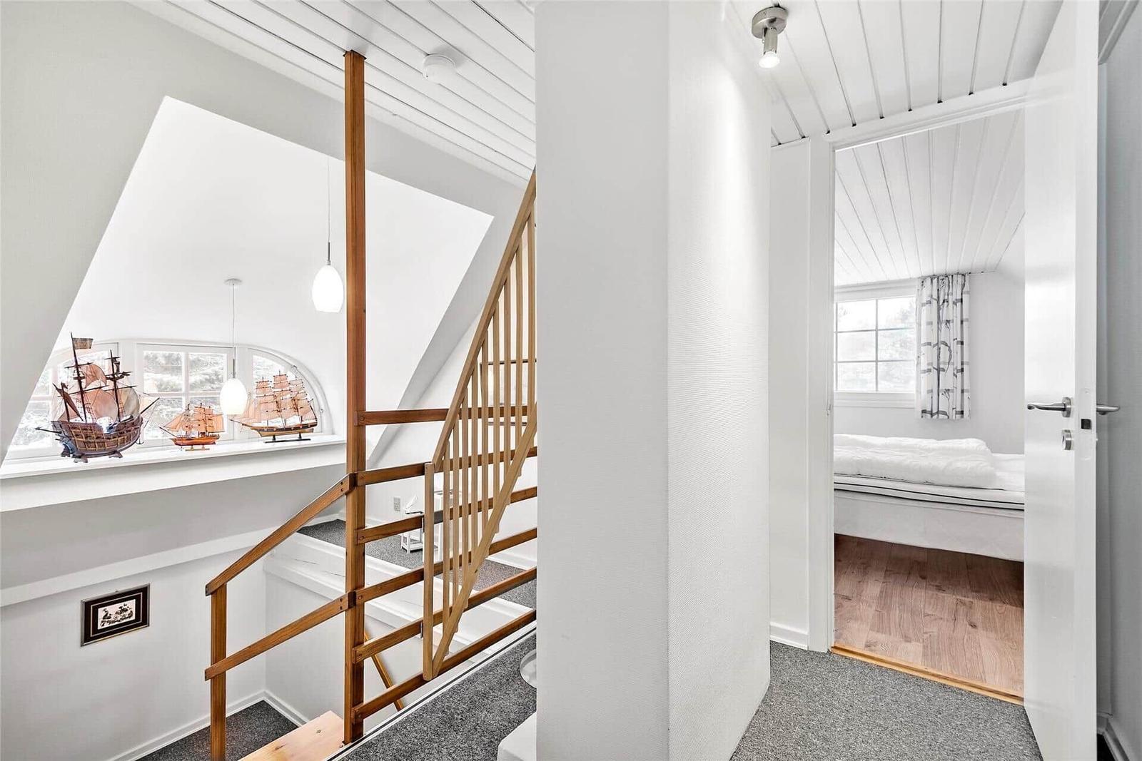 Schlafzimmer mit Dachschräge, Bett, zwei Stühlen und Fenster mit Vorhängen.
