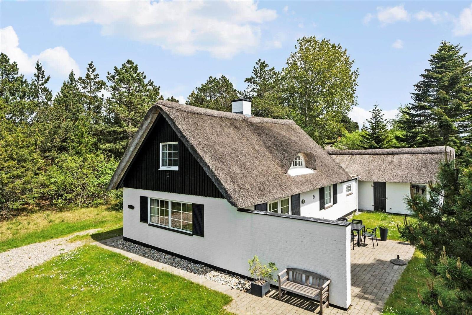 Haus mit Strohdach, Terrasse und Garten. Umgeben von Bäumen und Gras.