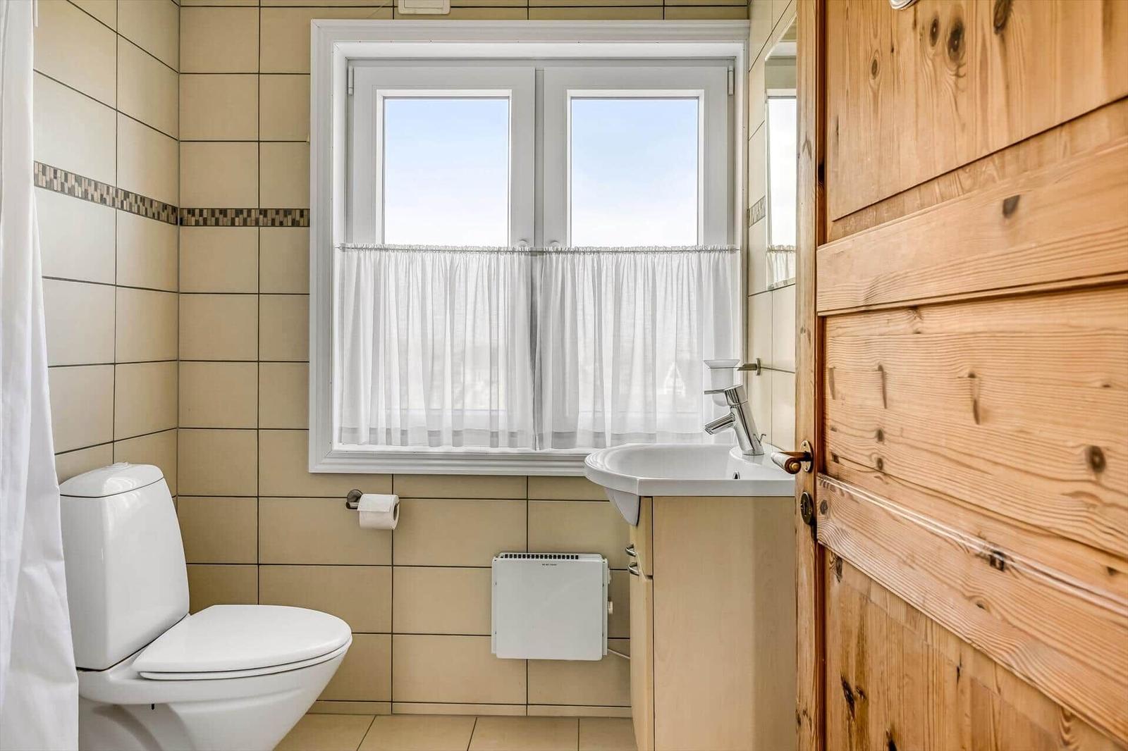 Durch das Fenster blickt man auf eine Landschaft mit Dünen und mehreren Häusern.