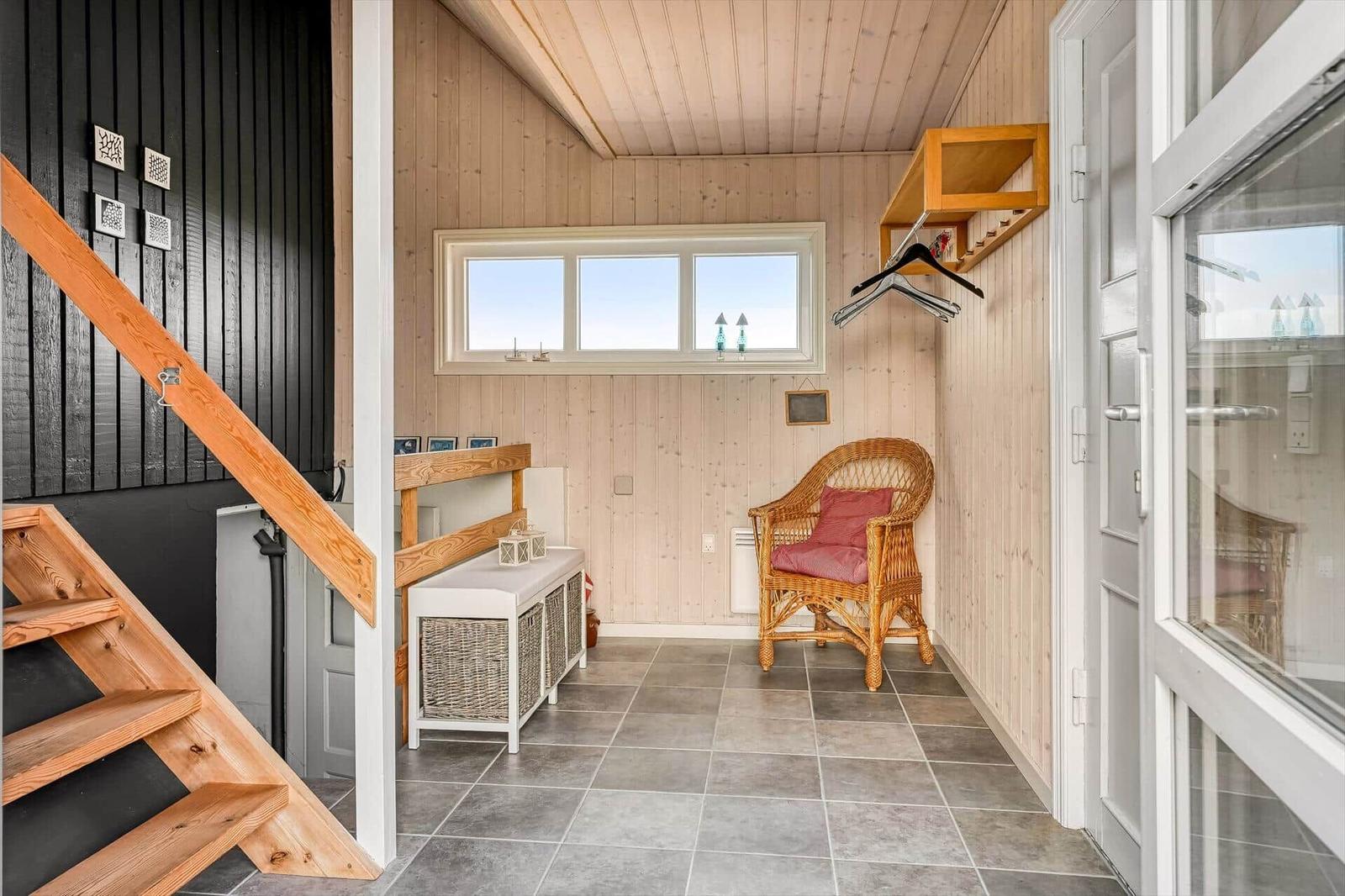 Ein dunkelgrauer Ferienhaus mit weißem Geländer und Terrasse in einer Dünenlandschaft.