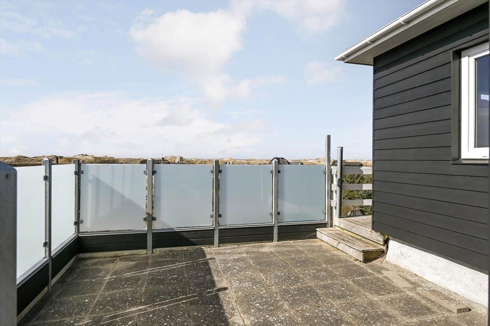 Durch das Fenster blickt man auf eine Siedlung zwischen Dünen und dem Meer.