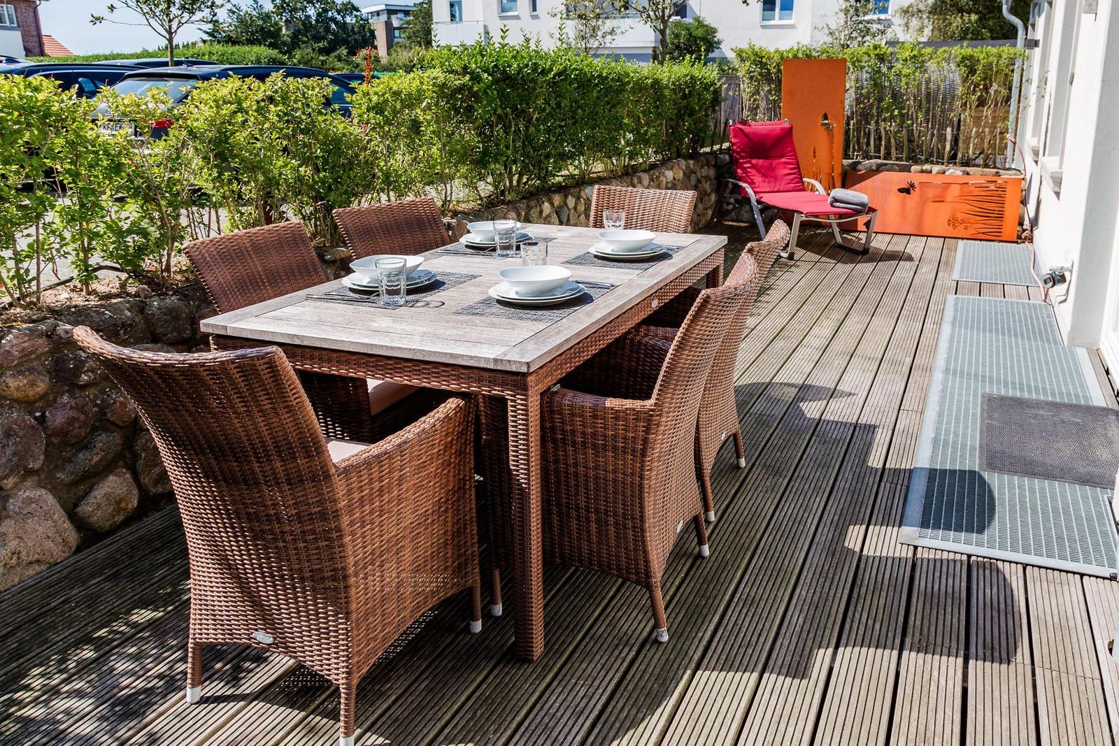 Roter Liegestuhl auf Holzterrasse mit Steinmauer und orangefarbenen Metallplatten.