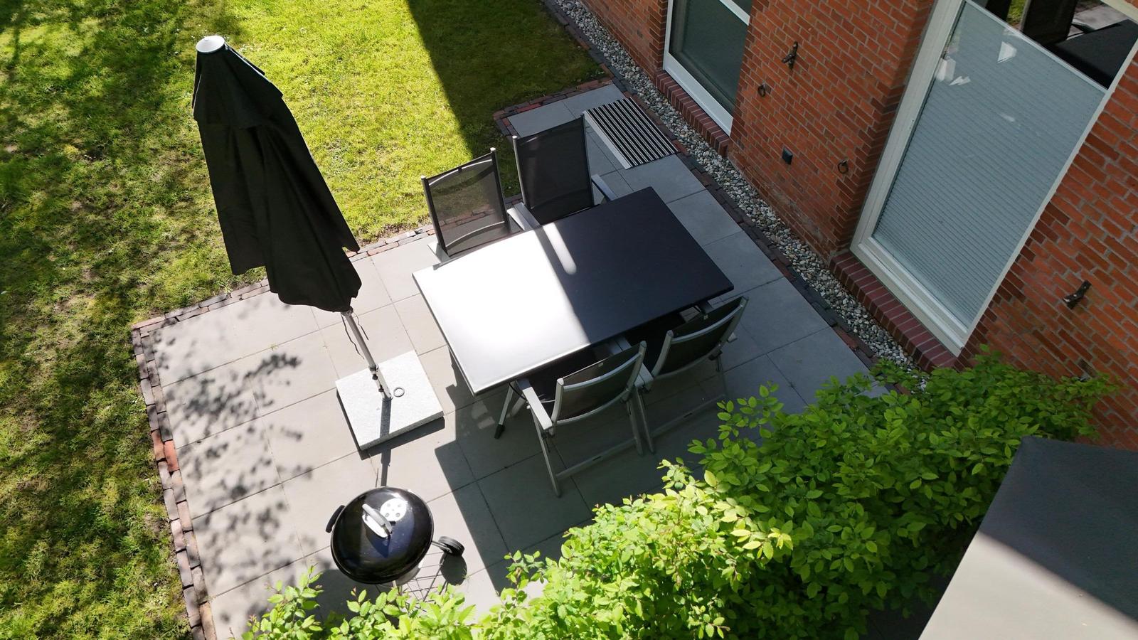 Rotes Ziegeldach, umgeben von Bäumen und Grünflächen. Gartenbereich mit Sitzmöbeln.