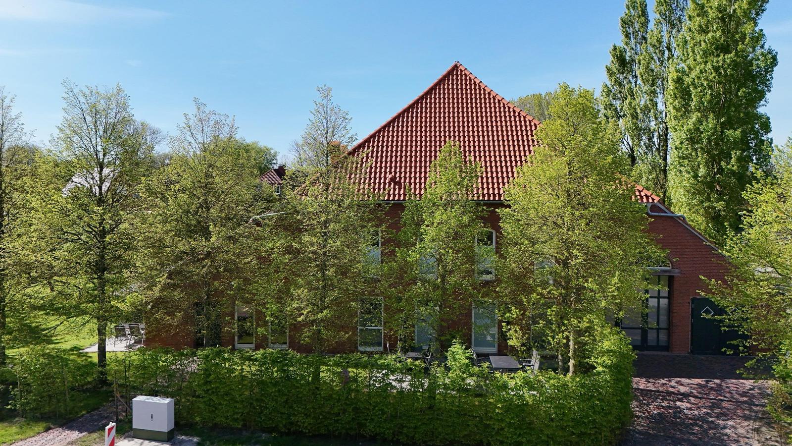 Terrasse mit zwei Sonnenschirmen, Sitzgelegenheiten und Grill. Roter Backsteinbau mit grüner Umgebung.
