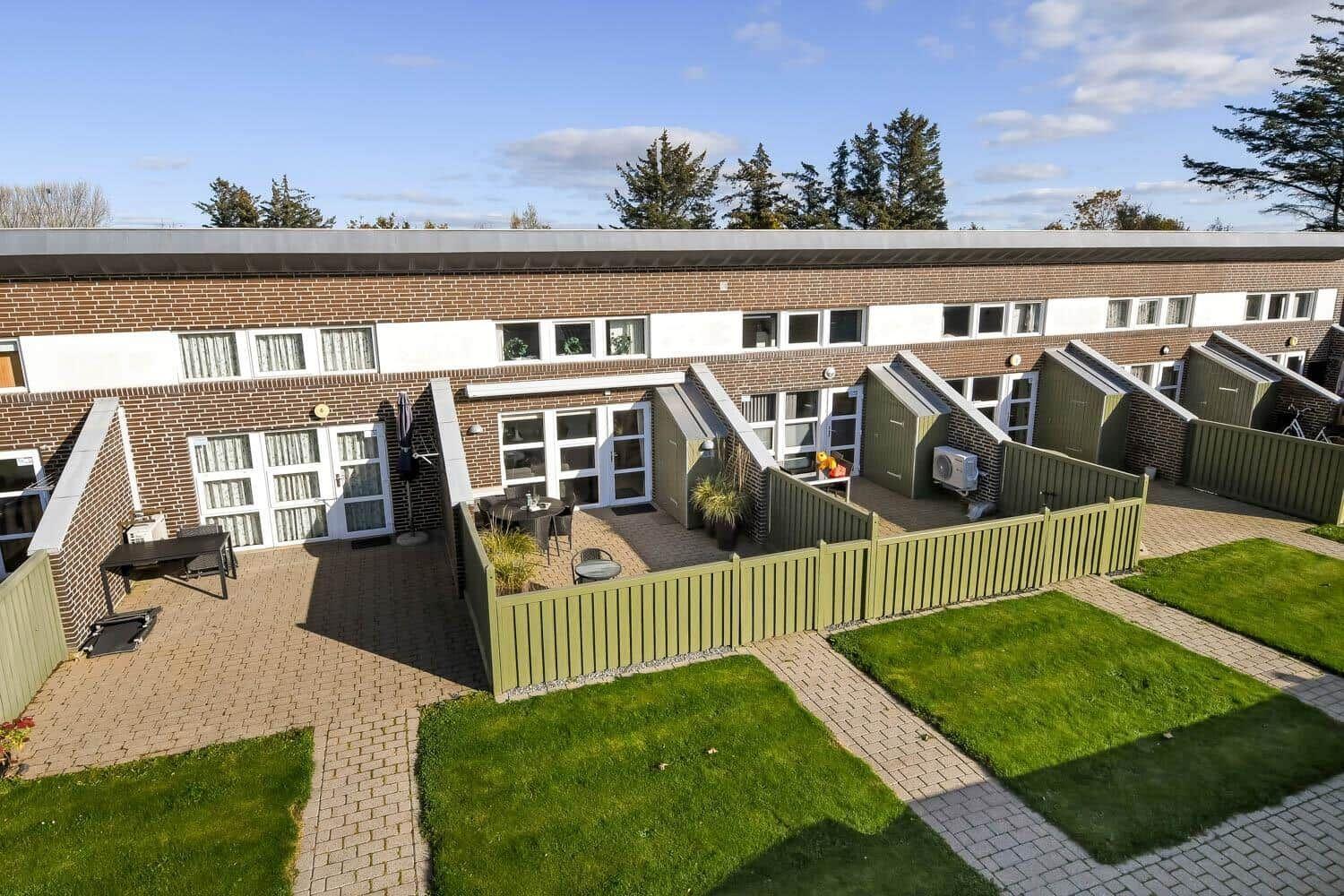 Haus mit braunem Backsteinfassade, grünem Zaun und gepflastertem Hof mit Garten.