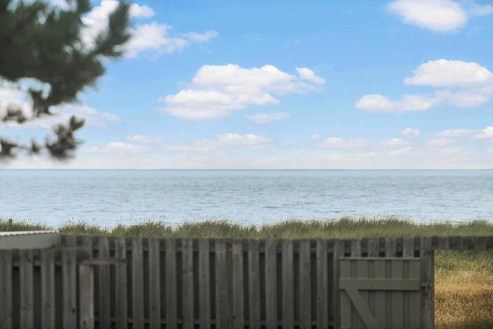 From a wooden fence, you can see the sea under a blue sky with white clouds.