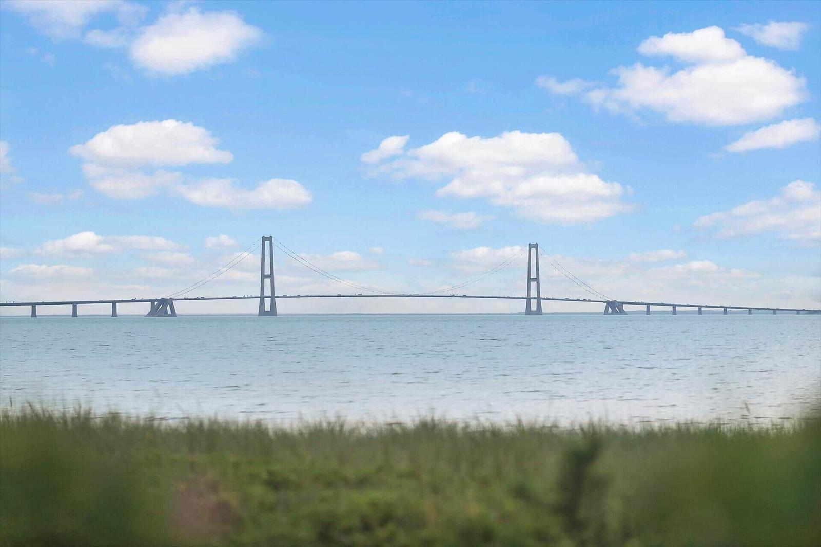 Harbor bridge over calm water under blue sky with white clouds.