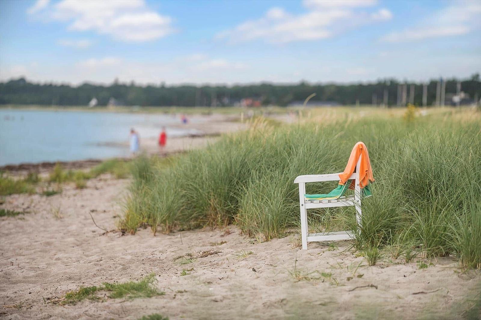 A white chair with an orange towel stands on sand beside grass.