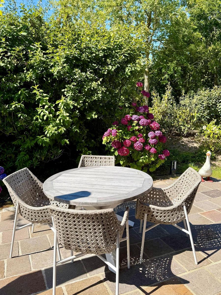 Terrasse mit Sonnenschutz, Tisch und Stühlen, umgeben von Pflanzen.