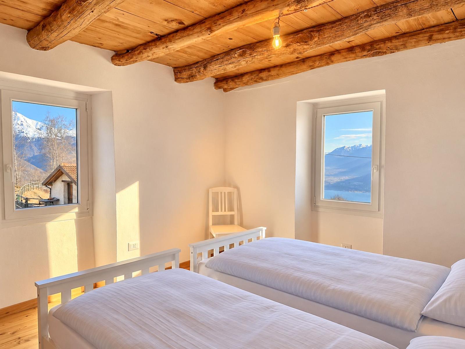 gemütliches Schlafzimmer mit verkleideter Holzdecke und toller Aussicht auf den See und die Bergkulisse