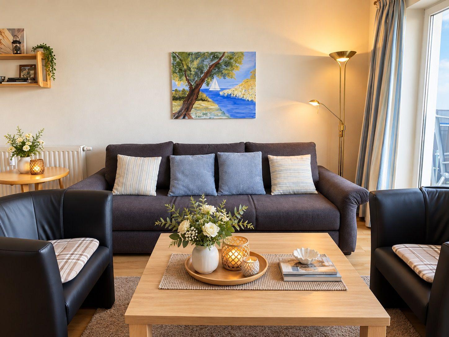 Wohnzimmer mit Sofa, Sessel, Couchtisch und Fernseher. Große Fenster mit Blick auf Balkon.