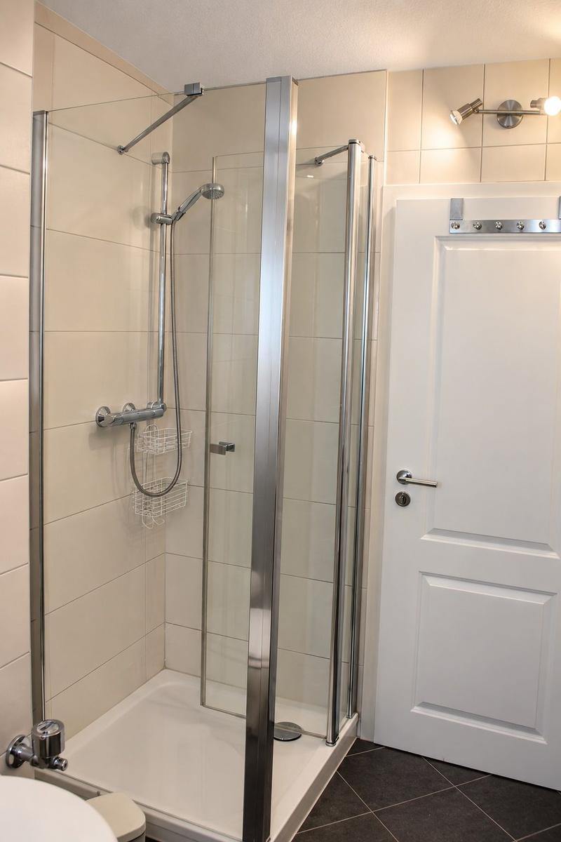 Dusche mit Glaswand, weiße Fliesen und Handtuch auf Boden