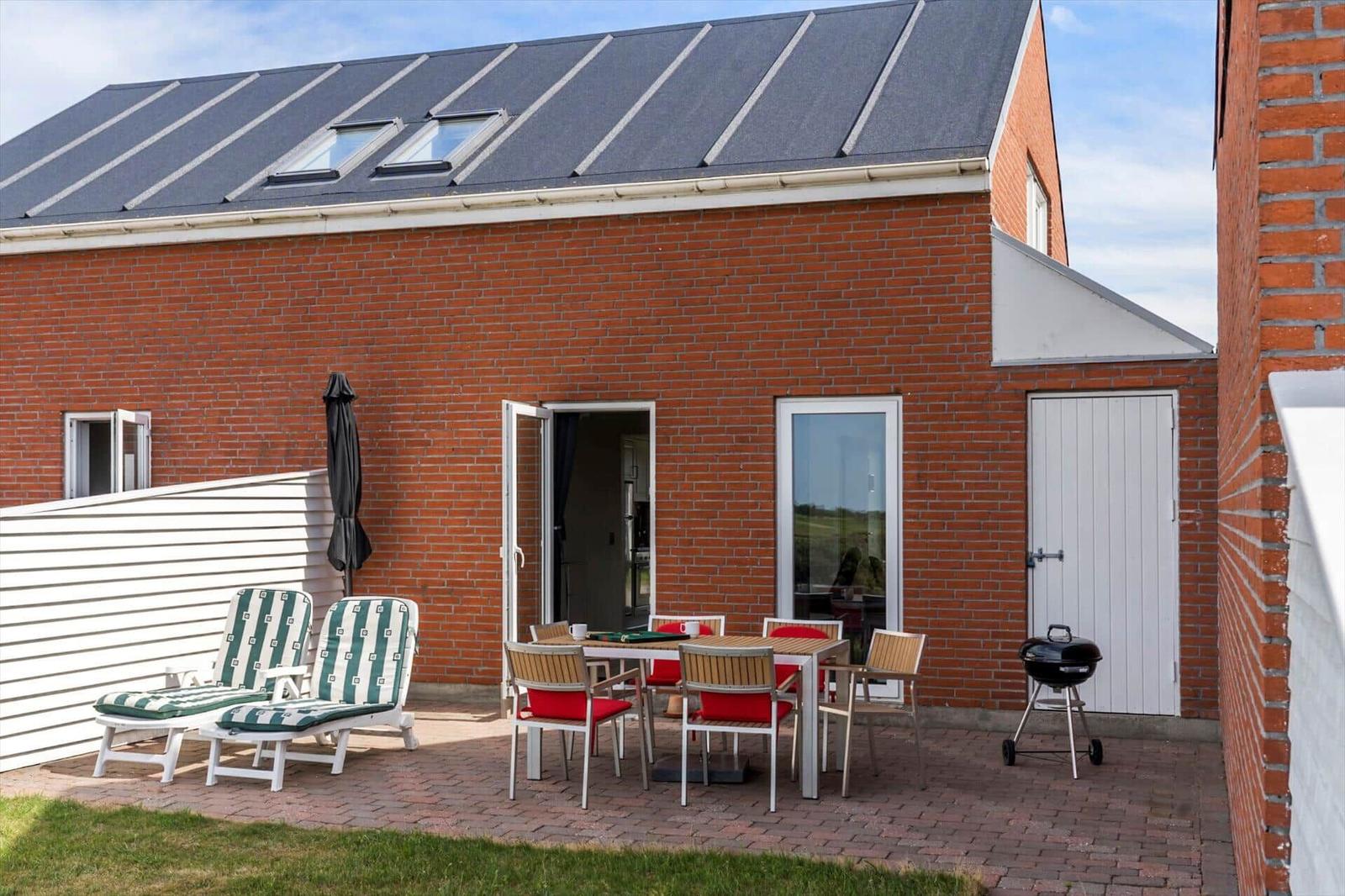 Terrasse mit Tisch und Stühlen, Blick auf Grasland und Sträucher.