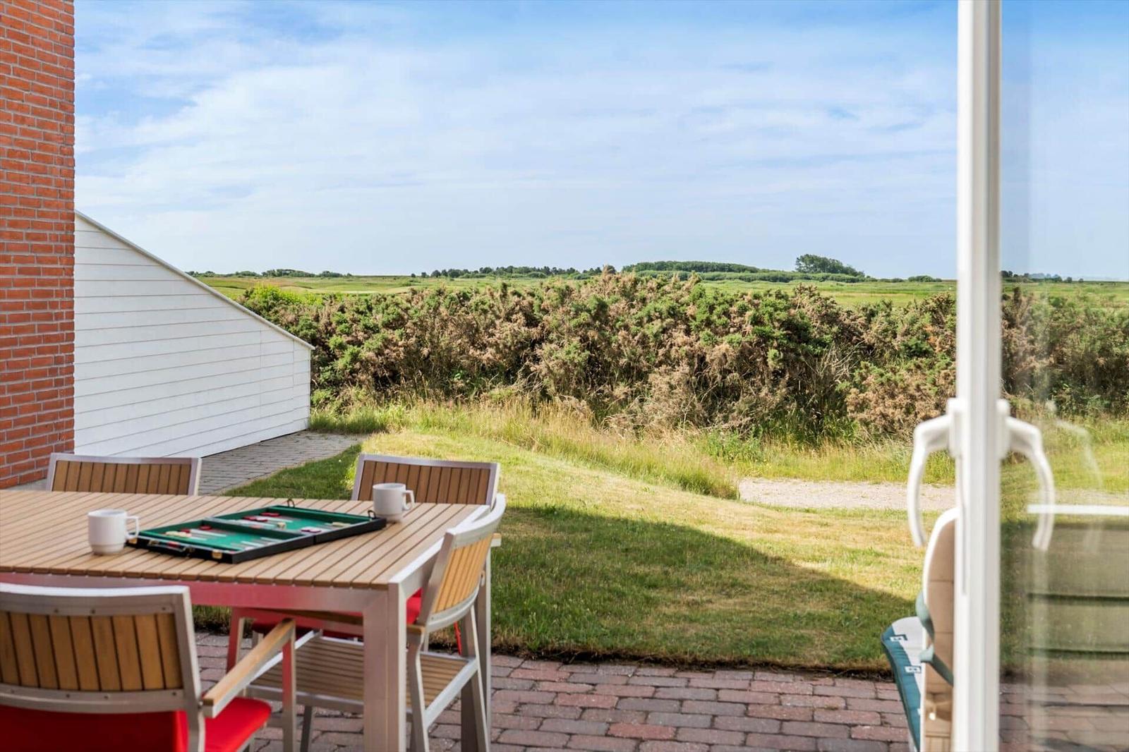 Roter Backsteinbau mit Terrasse, Gartenmöbeln und Grill. Tür führt ins Innere.