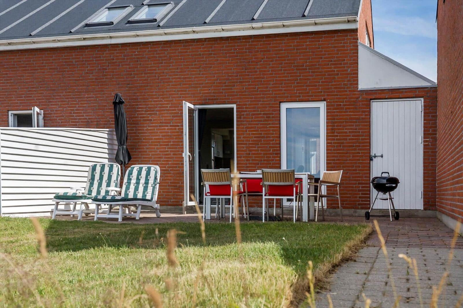 Terrasse mit Liegestühlen und Tisch. Blick auf Ferienhäuser und Spielplatz.