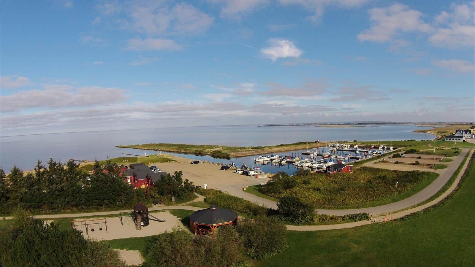 Hafen mit Booten, Strand, Spielplatz und Pavillon. Blick auf Wasser und grüne Landschaft.