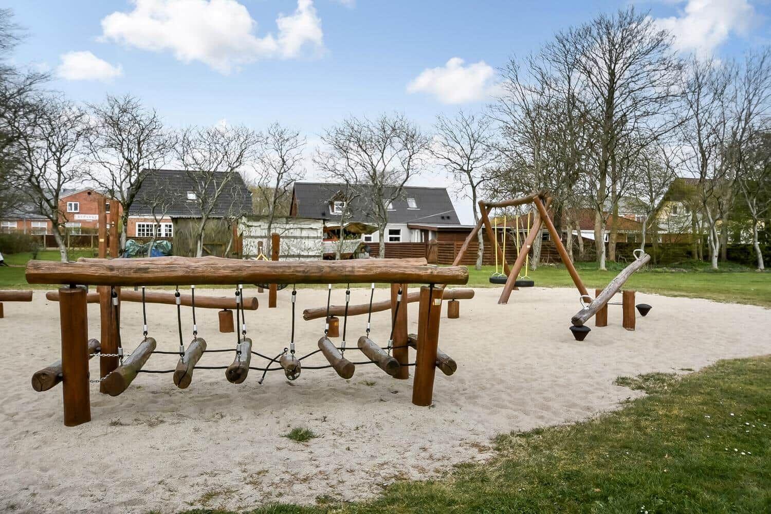 Holzspielplatz mit Sandfläche und Schaukelanlage im Hintergrund.