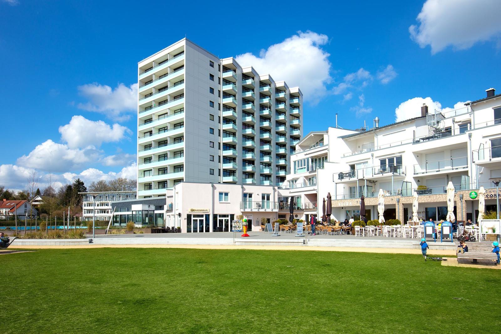Strand mit Liegestühlen und modernen Gebäuden im Hintergrund.
